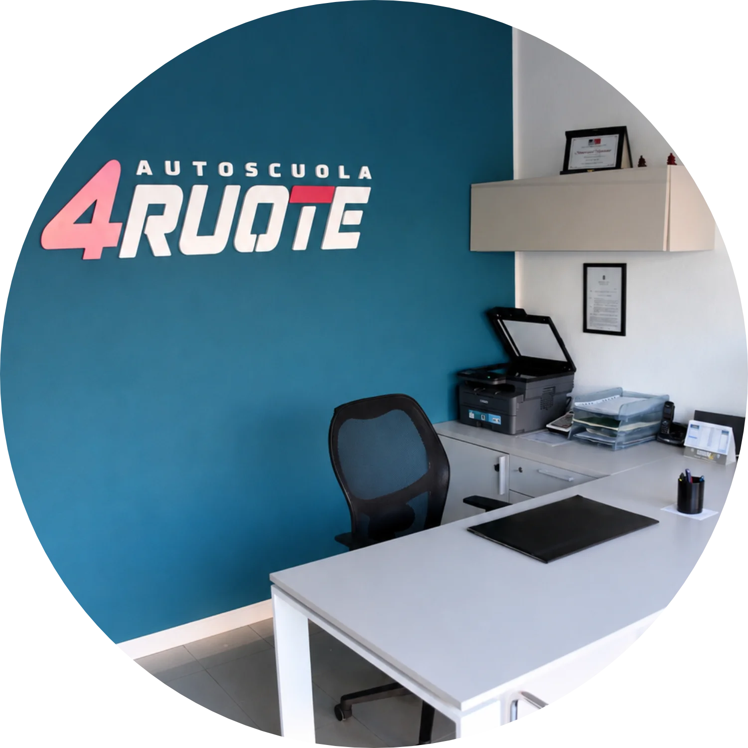 Sala accoglienza dell'Autoscuola 4 Ruote con scrivania e sedie per gli ospiti e logo a rilievo sulla parete di fondo.