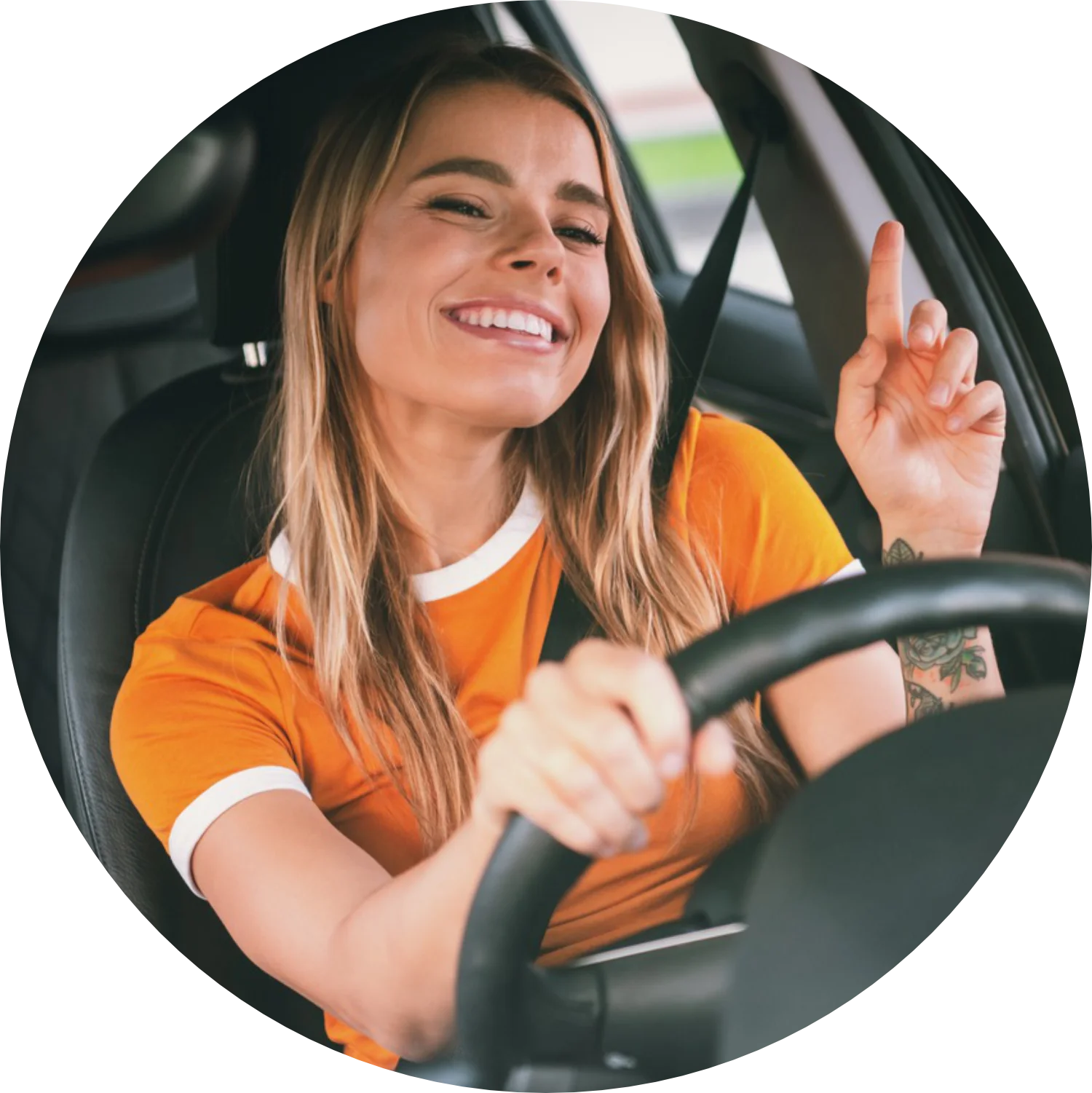 Ragazza bionda con maglia arancione seduta al posto di guida impugna il volante e sorride felice